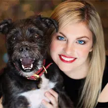 Smiling blonde woman holding a happy black dog with a red collar.